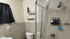 Un baño con ducha, inodoro, lavabo y cabina de ducha con mampara de vidrio.