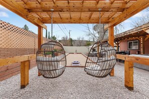 A wooden pergola with two swing seats and a table underneath.