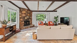 A living room with a stone fireplace, a sofa, a television, and a large window with curtains.