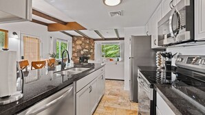 A modern kitchen with stainless steel appliances, a stone accent wall, and a large window providing a view of greenery.