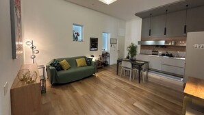 A modern living room with a green sofa, wooden flooring, and a dining area with a table and chairs. - Dimora Di Nardo "Geranio Apartment" — An elegant 75-square-meter apartment (Catania)