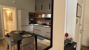 A modern kitchen with white cabinets, a dining table with chairs, and a mirror reflecting the space. - Dimora Di Nardo "Geranio Apartment" — An elegant 75-square-meter apartment (Catania)