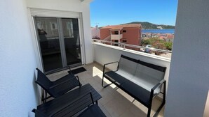 Een balkon met twee zwarte stoelen en een tafel, een schuifdeur en uitzicht op gebouwen en een wateroppervlak.