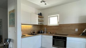 Een moderne keuken met witte kasten, een houten aanrechtblad en een ingebouwde oven. Er is een eethoek met een glazen tafel en stoelen.