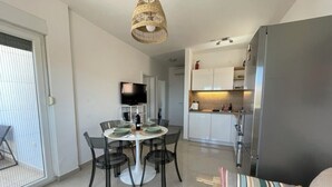 Een moderne keuken met een grote koelkast, een eethoek met een ronde tafel en stoelen, en een televisie op een dressoir.