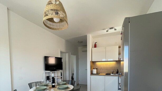 Een moderne woonkamer met een eethoek, een keuken en een grijze bank met gestreepte kussens.