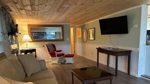 Ein Wohnzimmer mit Holzboden, einer Couch, einem Schaukelstuhl, einem Fernseher und einem Tisch.