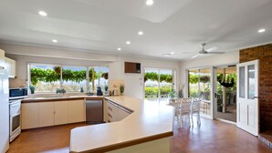 A modern kitchen with a large island, white cabinetry, and a view of greenery through the windows. - Monkey Gully Retreat - Pool - Mansfield - Sleeps 9 (Mansfield)
