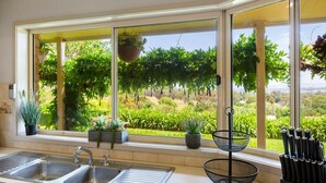 A kitchen with a large window overlooking a garden, a sink, and a knife rack. - Monkey Gully Retreat - Pool - Mansfield - Sleeps 9 (Mansfield)