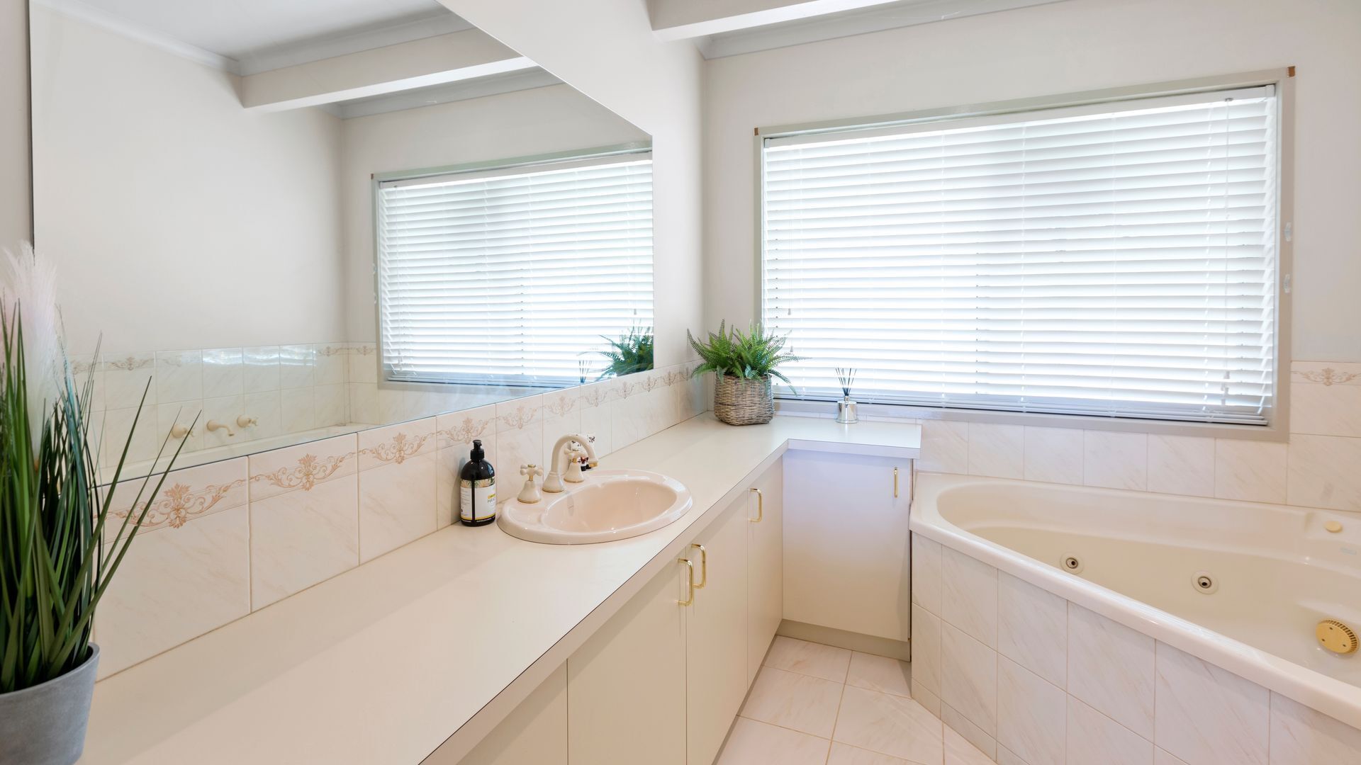 A modern bathroom with a double sink, a bathtub, and two windows with blinds.