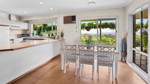 A modern kitchen with white cabinets, a wooden countertop, and a dining area with white chairs and a table. - Monkey Gully Retreat - Pool - Mansfield - Sleeps 9 (Mansfield)
