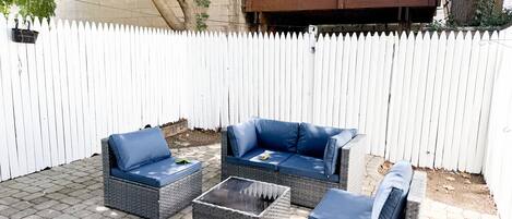 Une terrasse avec des meubles en osier et une clôture blanche en bois.