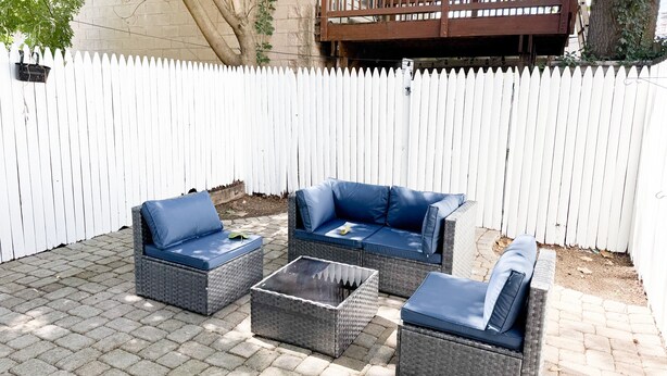 Une terrasse avec des meubles en osier et une clôture blanche en bois.