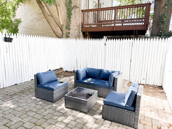 Une terrasse avec des meubles en osier et une clôture blanche en bois.
