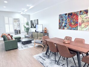 Uma sala de estar moderna com área de jantar, janelas amplas e obras de arte na parede.