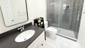 Une salle de bain moderne avec un lavabo blanc, un plan de toilette noir et une douche séparée par des parois en verre.