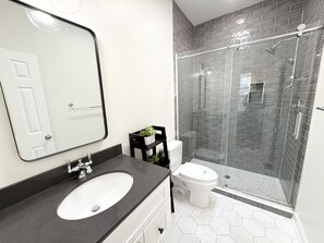 Une salle de bain moderne avec un lavabo blanc, un plan de toilette noir et une douche séparée par des parois en verre.