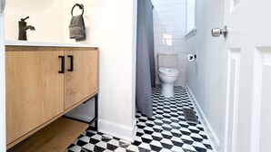 Une salle de bain avec un meuble-lavabo en bois, un miroir, une serviette, des toilettes et un carrelage décoratif.