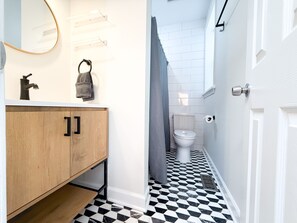 Une salle de bain avec un meuble-lavabo en bois, un miroir, une serviette, des toilettes et un carrelage décoratif.