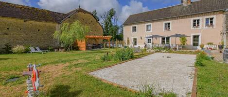 A courtyard with a gravel area, a wooden pergola, and a stone building with a tiled roof.