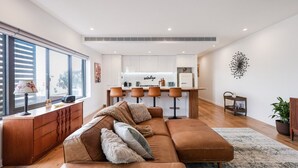 A modern living room with a brown leather sectional sofa, a wooden coffee table, and a large window with blinds.