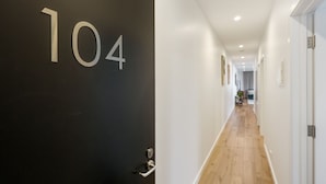 A hallway with a black door labeled '104', wooden flooring, white walls, and recessed ceiling lights.