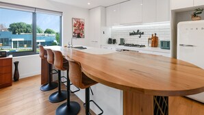 A modern kitchen with a large island, bar stools, white cabinetry, and a view of the outside.
