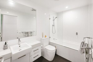 Un baño moderno con lavamanos, espejo, inodoro y bañera blancos.