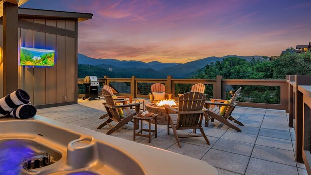 Un jacuzzi con vistas a montañas, mobiliario exterior con sillas Adirondack y un televisor en una pared de madera.