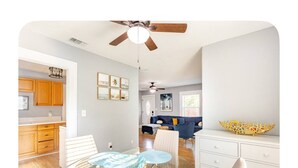 A modern kitchen with wooden cabinets, a dining area with a glass table and chairs, a blue sofa, and a white dresser with a decorative bowl.