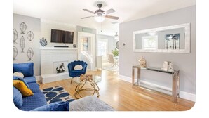 A modern living room with a fireplace, a ceiling fan, and a dining area with a glass table and metal frame.