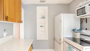 A compact kitchen with wooden cabinets, a white countertop, a built-in microwave, and a stove.