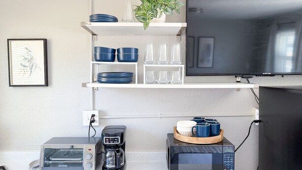A compact kitchen with a microwave, toaster, coffee maker, and a TV mounted on the wall. - Olde Town Arvada Tiny Retreat (Arvada)