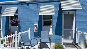 A blue building with white shutters, a white picket fence, and two chairs on the porch. - Olde Town Arvada Tiny Retreat (Arvada)
