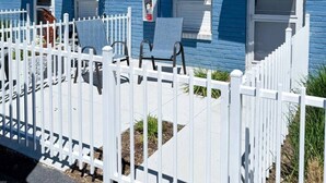 A blue building with white shutters, a white picket fence, and a small porch with two chairs. - Olde Town Arvada Tiny Retreat (Arvada)