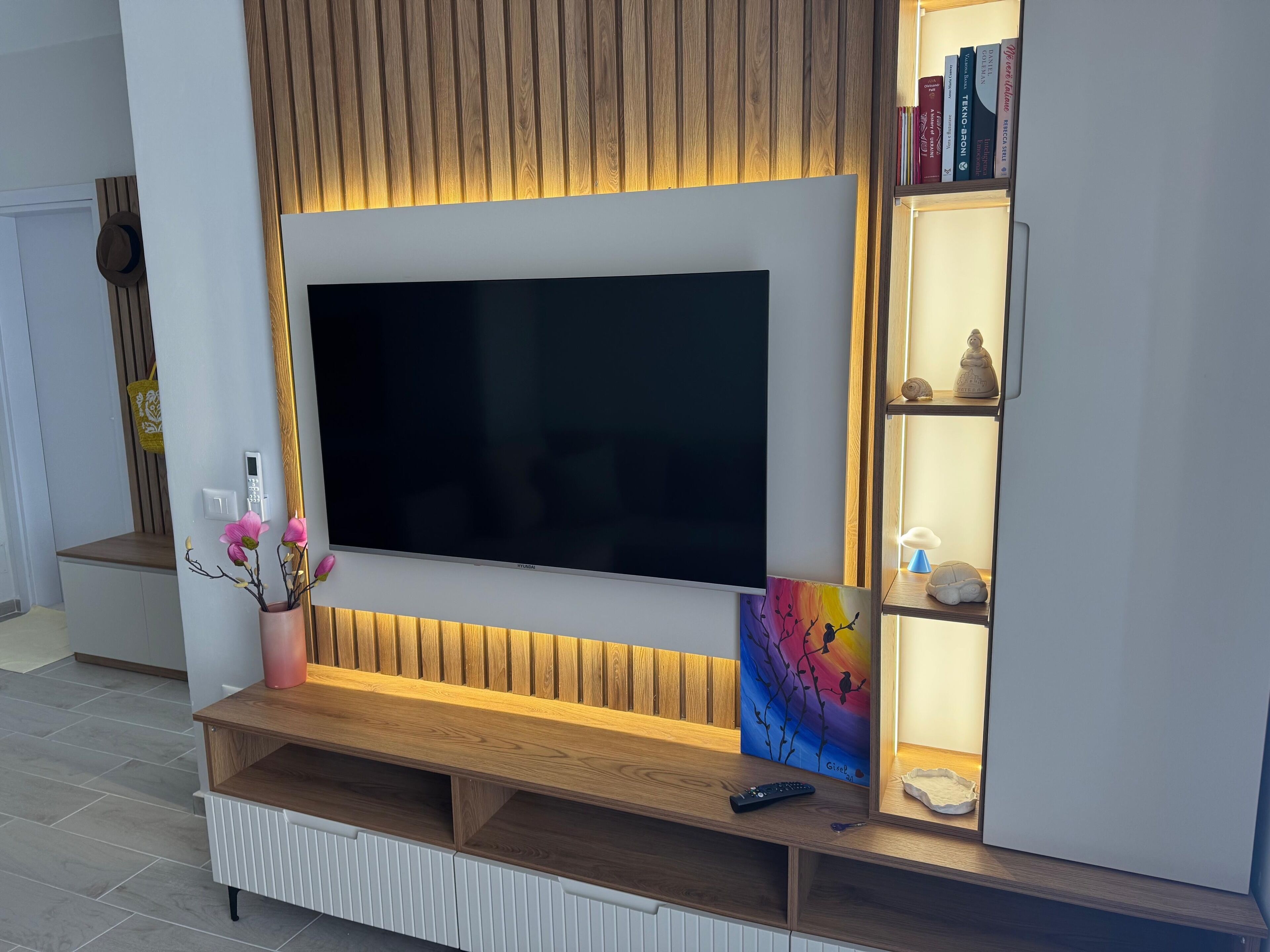 A modern entertainment unit with a large flat-screen TV, wooden shelves, and a small shelf with decorative items.