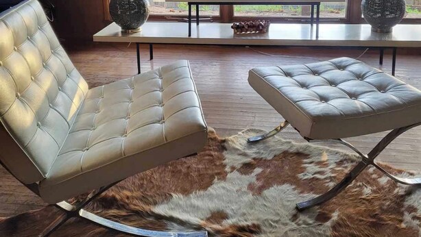 A modern living room with a leather sofa, a matching ottoman, two lamps, and a large window overlooking a forested area. - Mountain Escape Near RMNP, Views, River Access, Dogs OK (Drake)