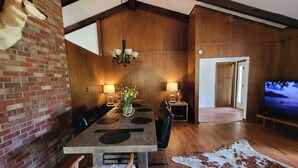 A dining area with a wooden table, chairs, and a chandelier. There is a television in the background and a door leading to another room. - Mountain Escape Near RMNP, Views, River Access, Dogs OK (Drake)