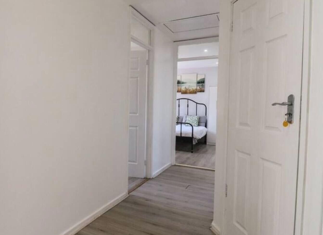A hallway with a bed in the background, a white door on the right, and a white wall on the left.