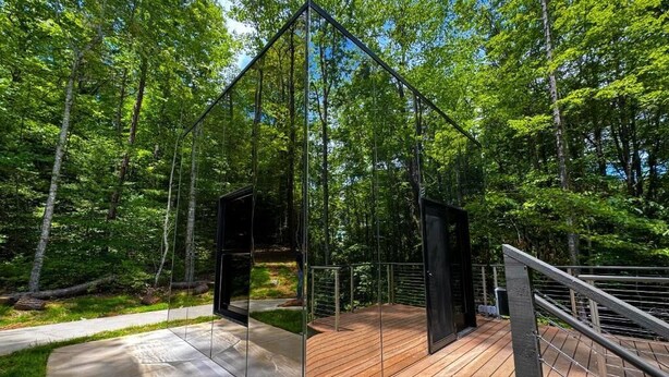 A modern outdoor deck with glass walls, surrounded by a forest. - Mirror Cabin - Reflections (Balsam Grove)