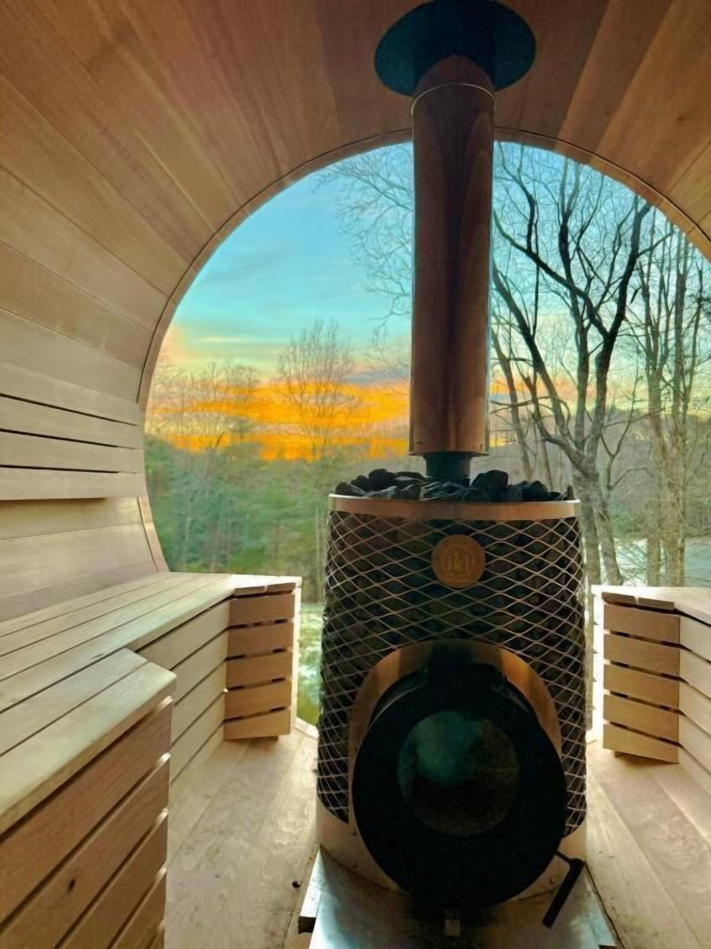 A sauna with a large window, wooden benches, and a central heating unit.