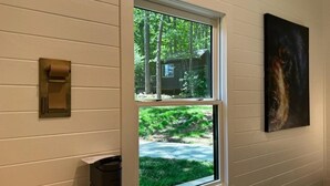 A window with a view of a cabin, a painting on the wall, and a coffee maker on the floor. - Mirror Cabin - Reflections (Balsam Grove)