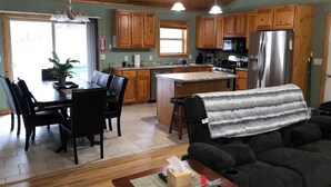 A spacious kitchen with wooden cabinets, a dining area with a table and chairs, and a living room with a sofa. - Rome Ranch Retreat: Golf + Lake + Pool + ATV + Dog + Disc & Foot Golf too! (Nekoosa)