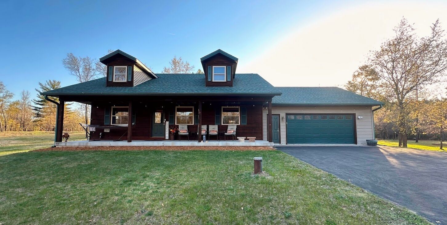 A two-story log cabin with a covered porch, a garage, and a well-maintained lawn.