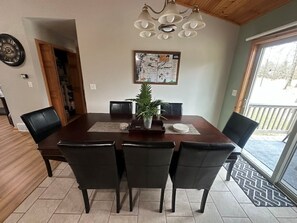 Uma área de refeições com mesa de madeira, cadeiras pretas, uma planta em vaso e um mapa na parede.
