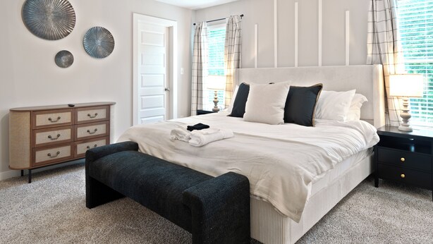 Een slaapkamer met een groot bed, een bankje, een dressoir en decoratieve wanddecoratie.