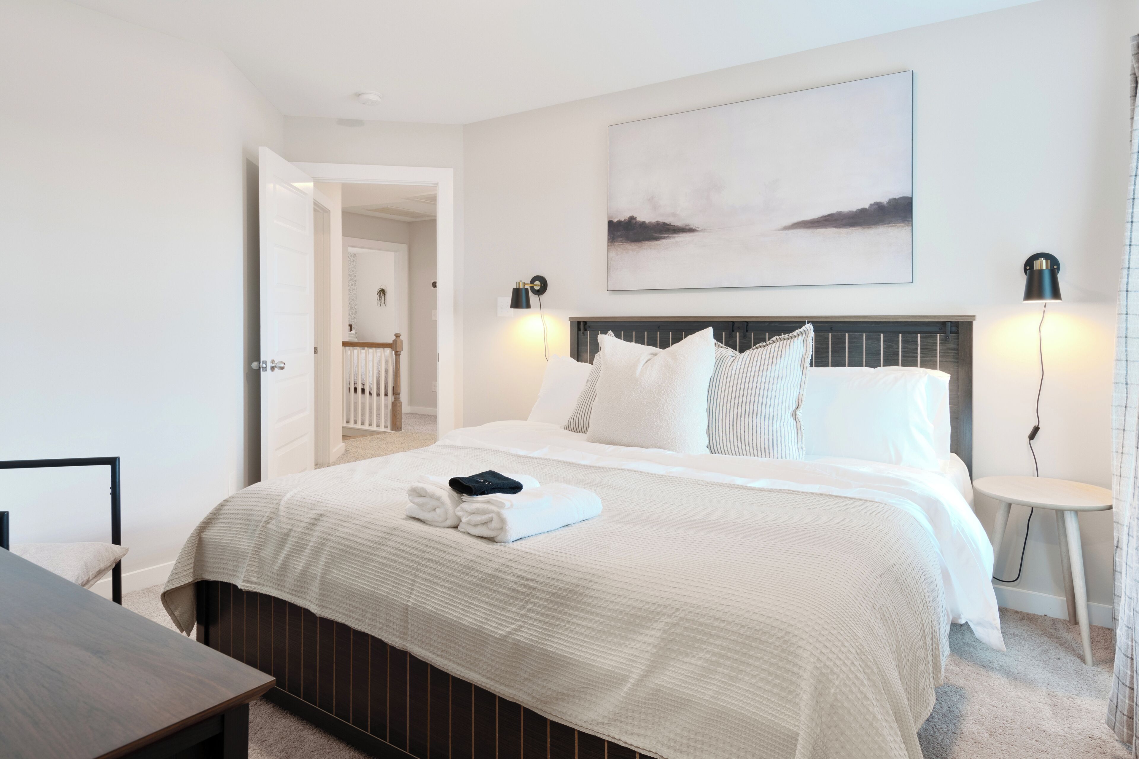 Una habitación de hotel moderna con una cama grande, una mesita de noche, una pequeña mesa redonda y un cuadro en la pared.