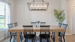 Een eetkamer met een houten tafel, zwarte stoelen, een kroonluchter en een kamerbreed tapijt.