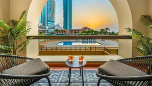 Ein Balkon mit Korbstühlen, einem kleinen Tisch und Blick auf eine Skyline mit hohen Gebäuden und einem Pool.
