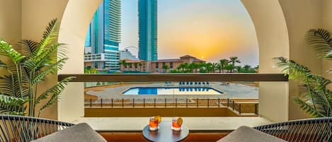 A balcony with wicker chairs, a small table, and a view of a cityscape with tall buildings and a pool.